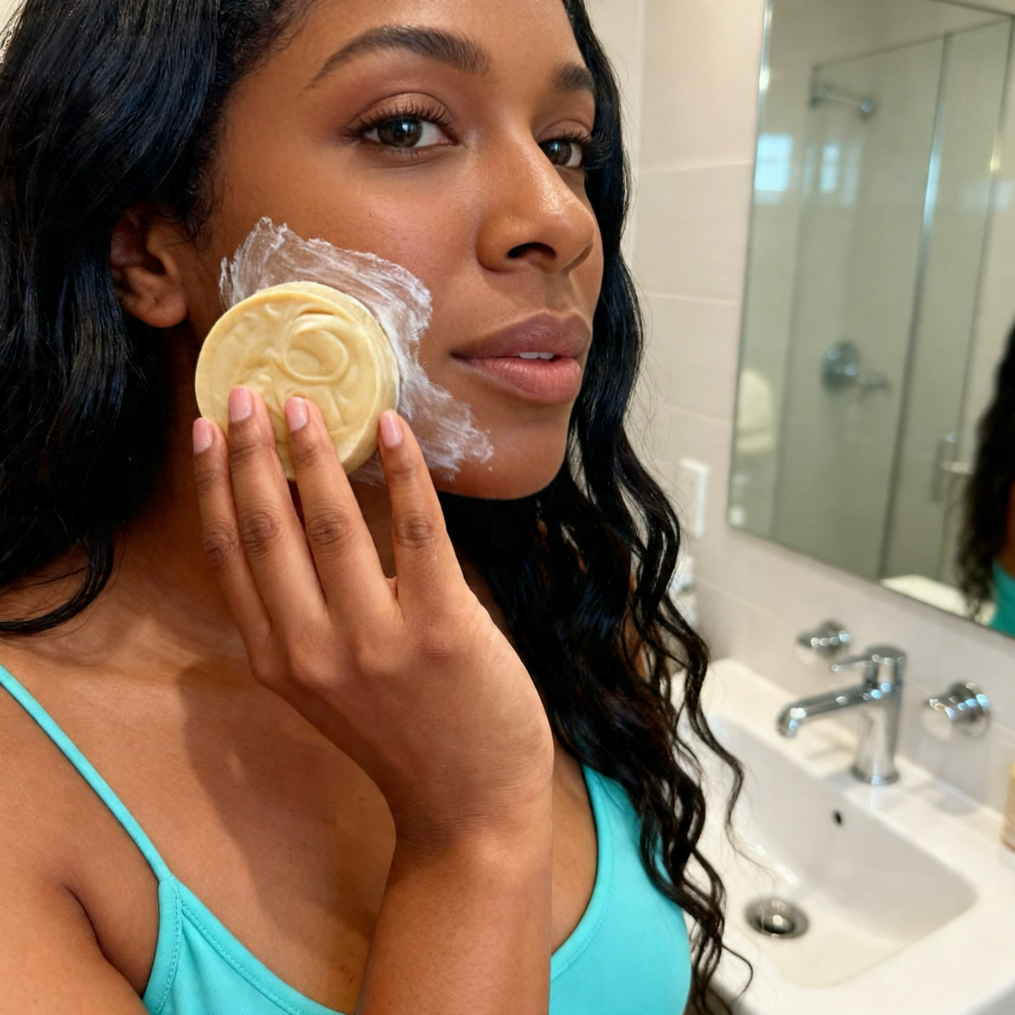 Woman applying soap to her face in a bathroom.